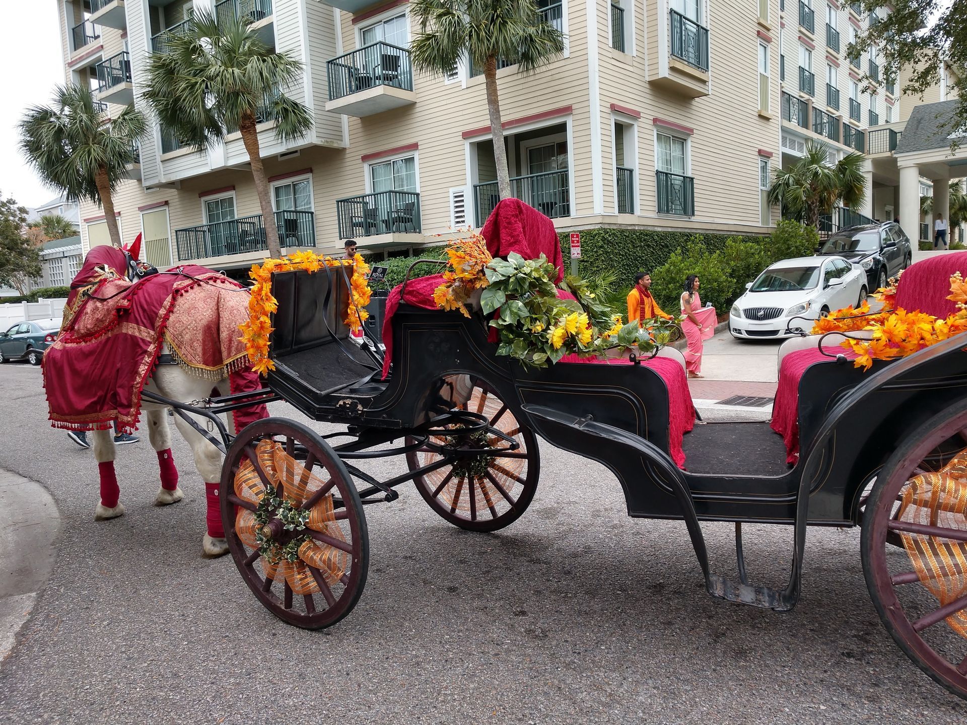 Decorated horse-drawn carriages with red and orange flowers on a city street near apartment buildings