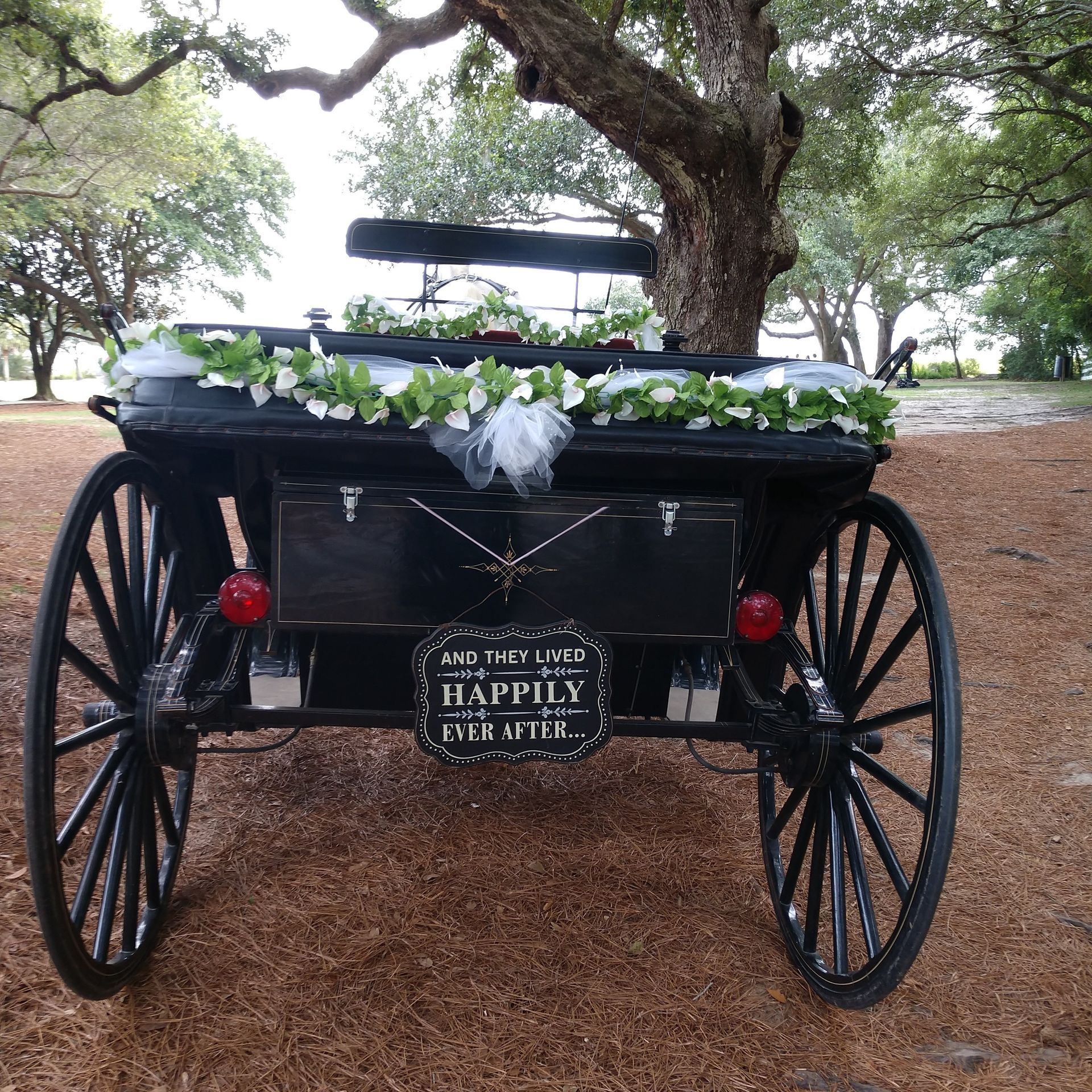 Black carriage with white flowers and a “happily ever after” sign under a tree outdoors