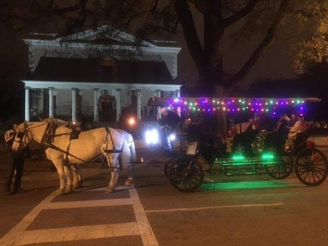 Horse-drawn carriage lit with colorful lights on a street at night, passing a building in the background