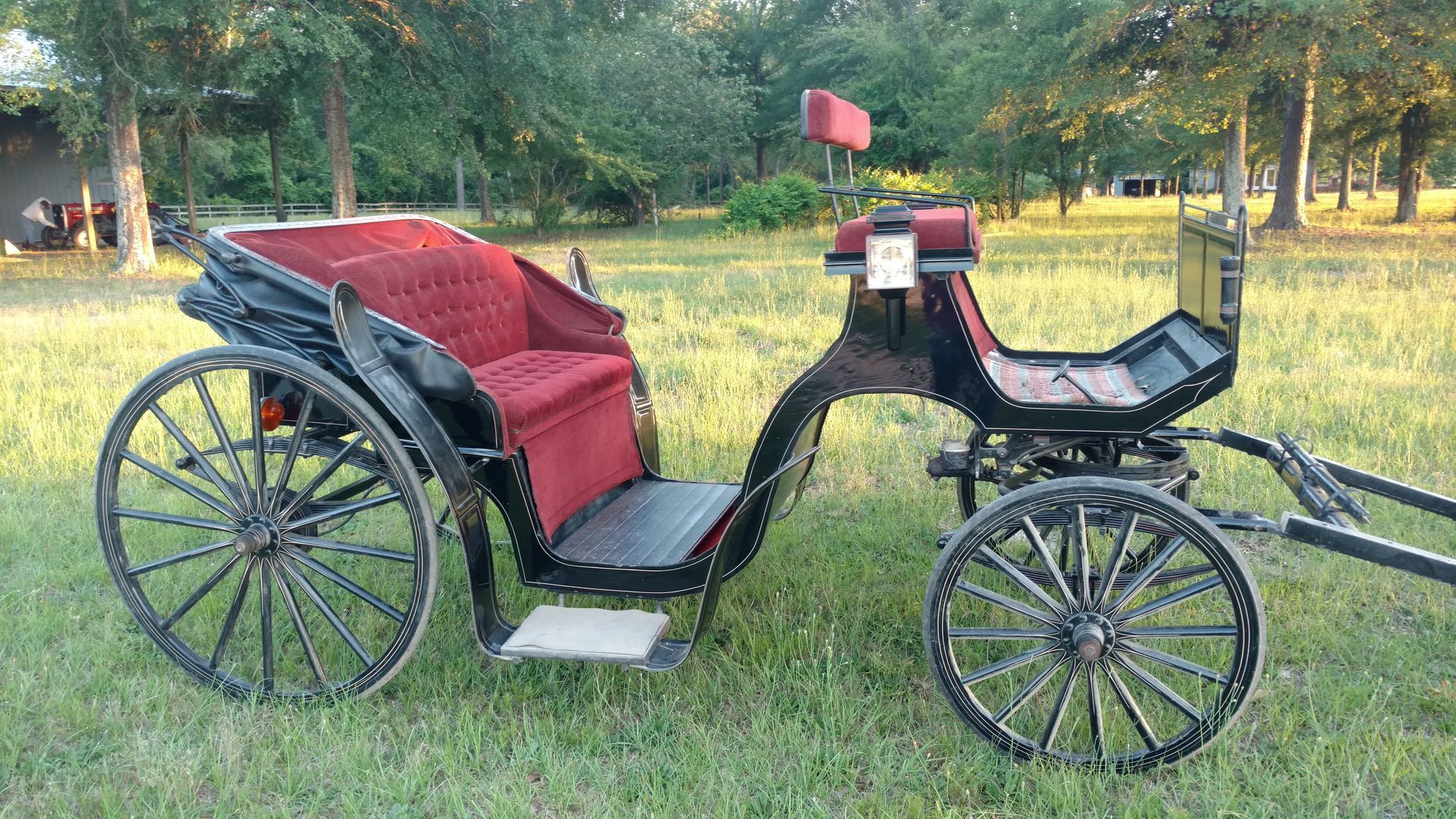 Vintage black-and-red horse carriage on grass, side view with large spoked wheels and red upholstered seat.