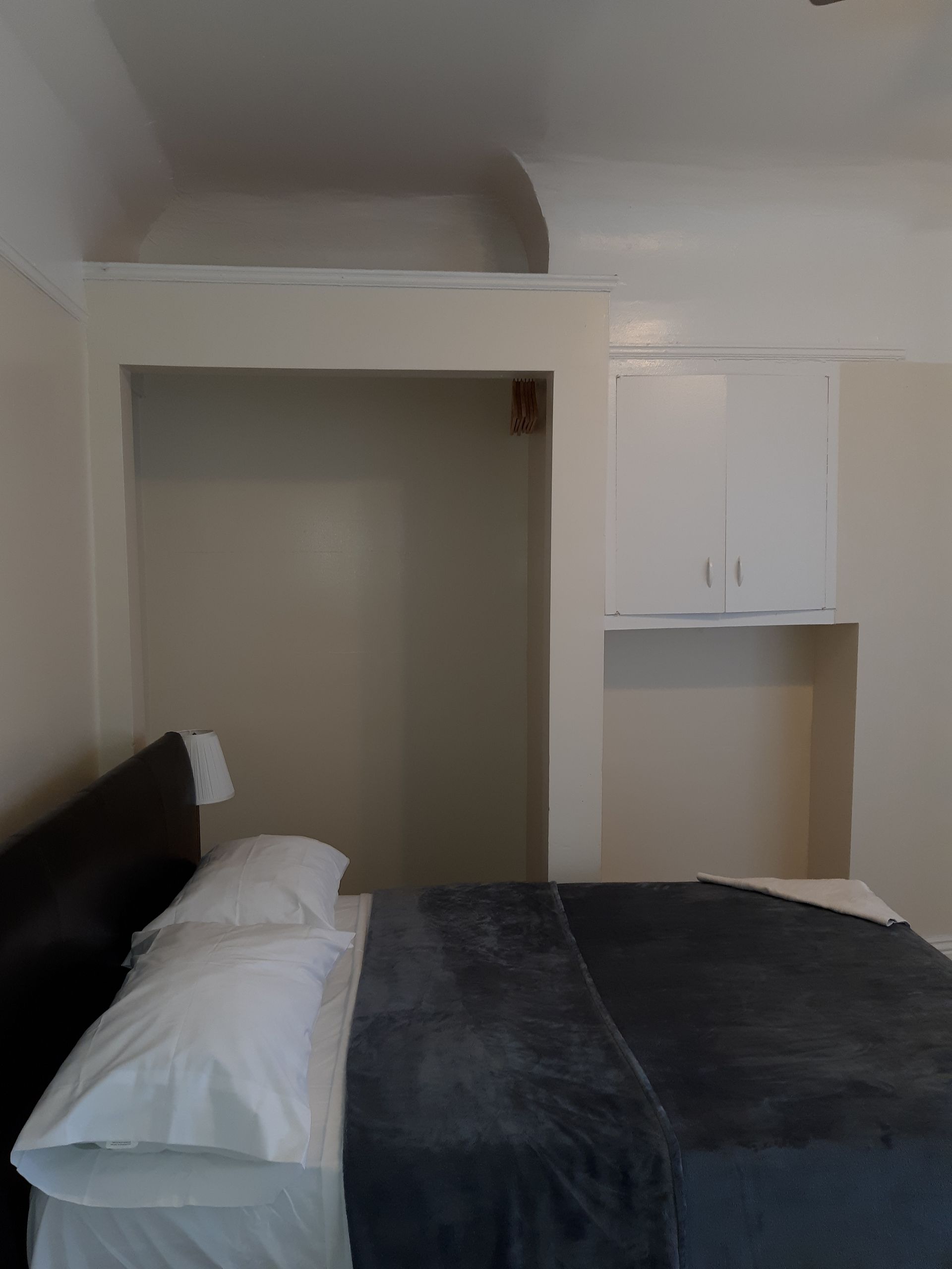 A bedroom with a bed and a shelf above it