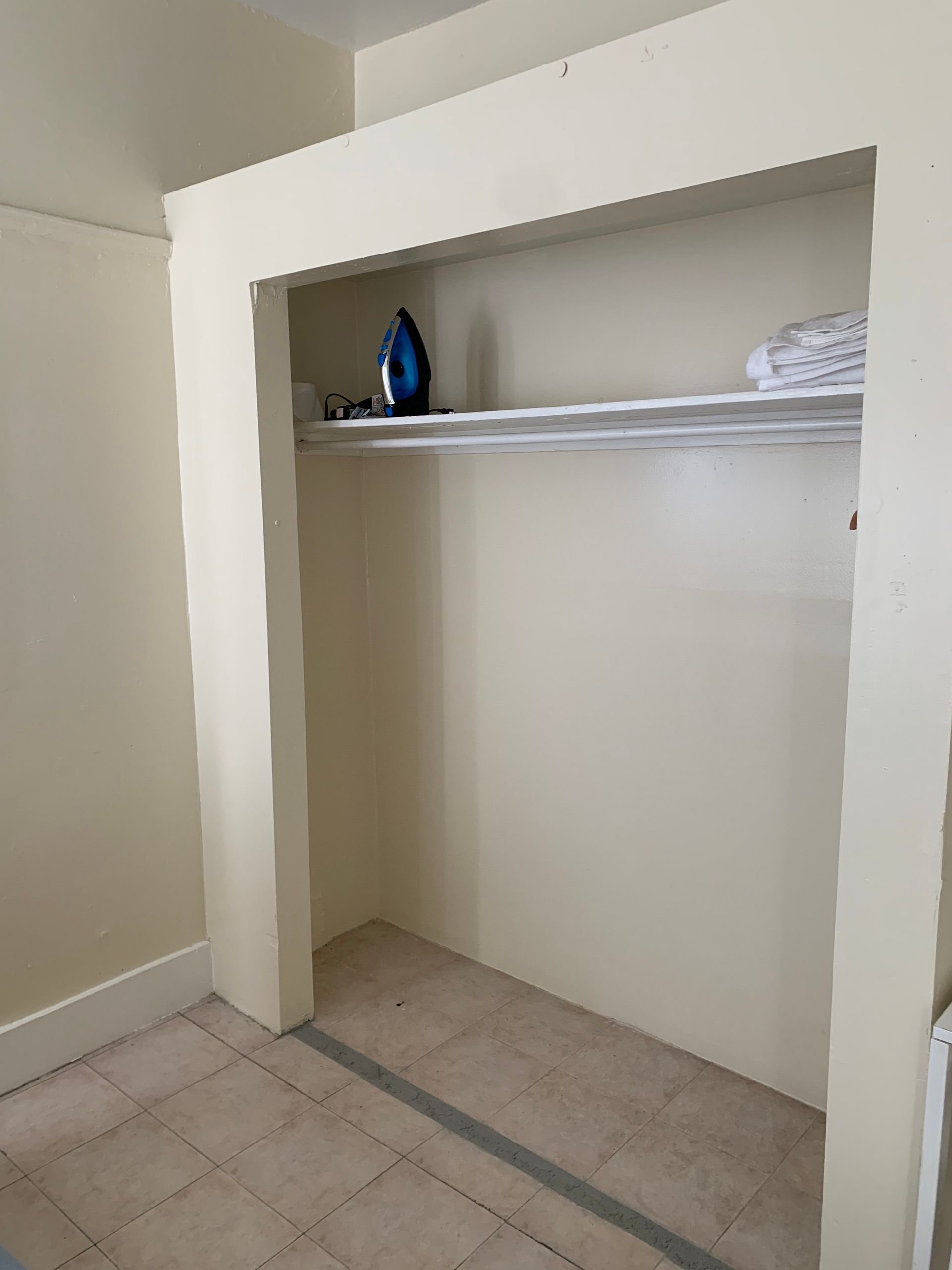 A closet with a shelf and a blue iron on top of it.