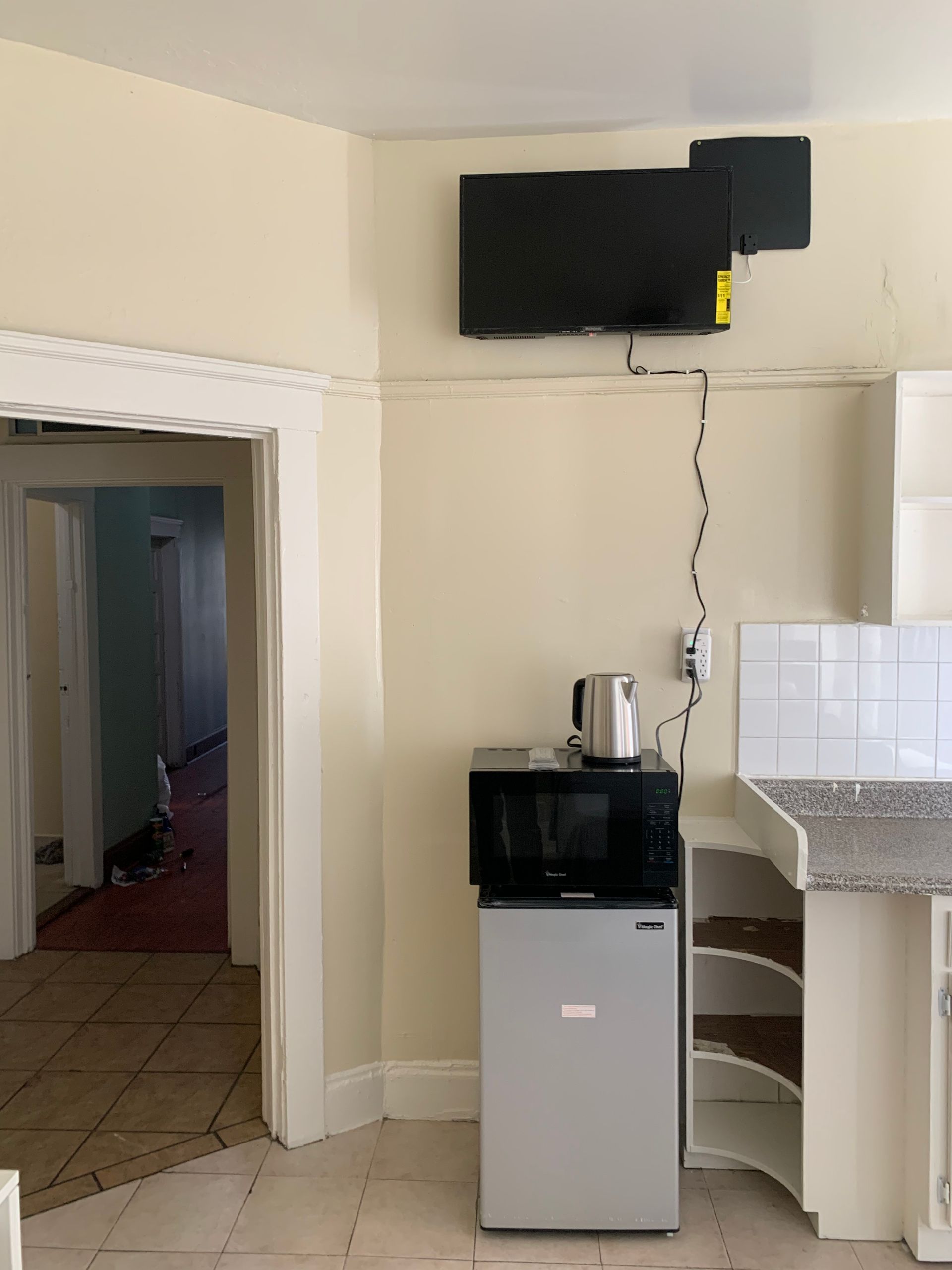 A kitchen with a small refrigerator a microwave and a flat screen tv