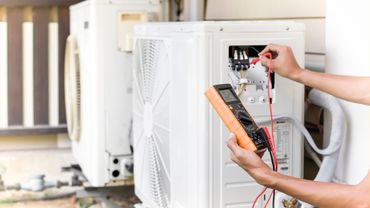 Technician testing wiring in an outdoor air conditioning unit with a multimeter