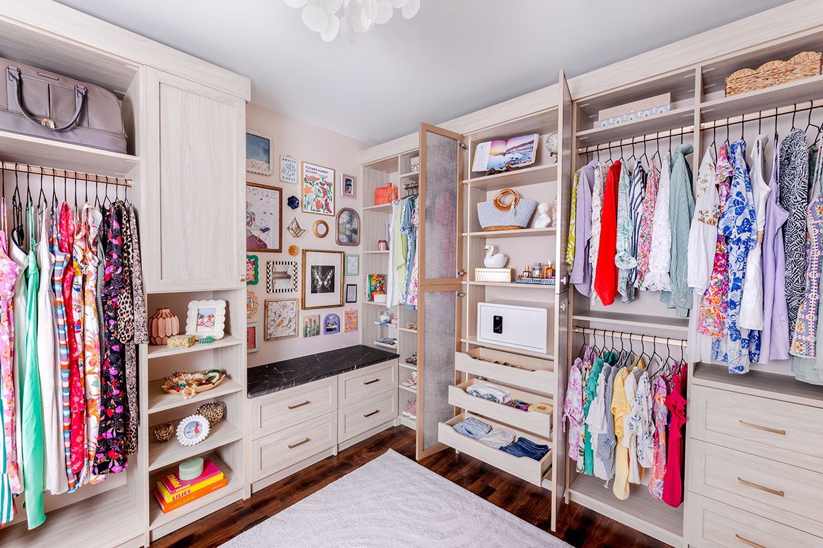 Bright walk-in closet with organized clothes, shelves, drawers, and framed wall art.