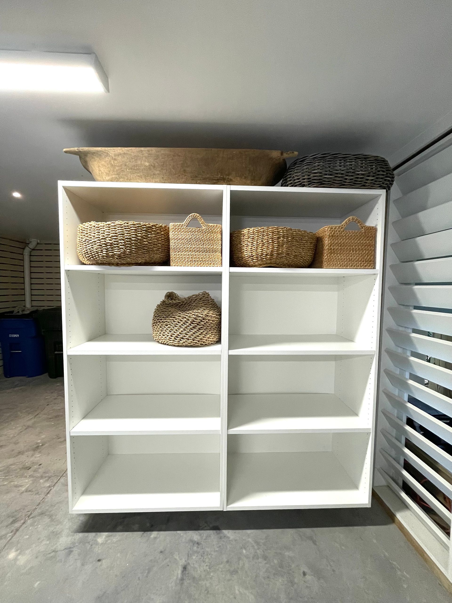A white shelf with baskets on it in a room.
