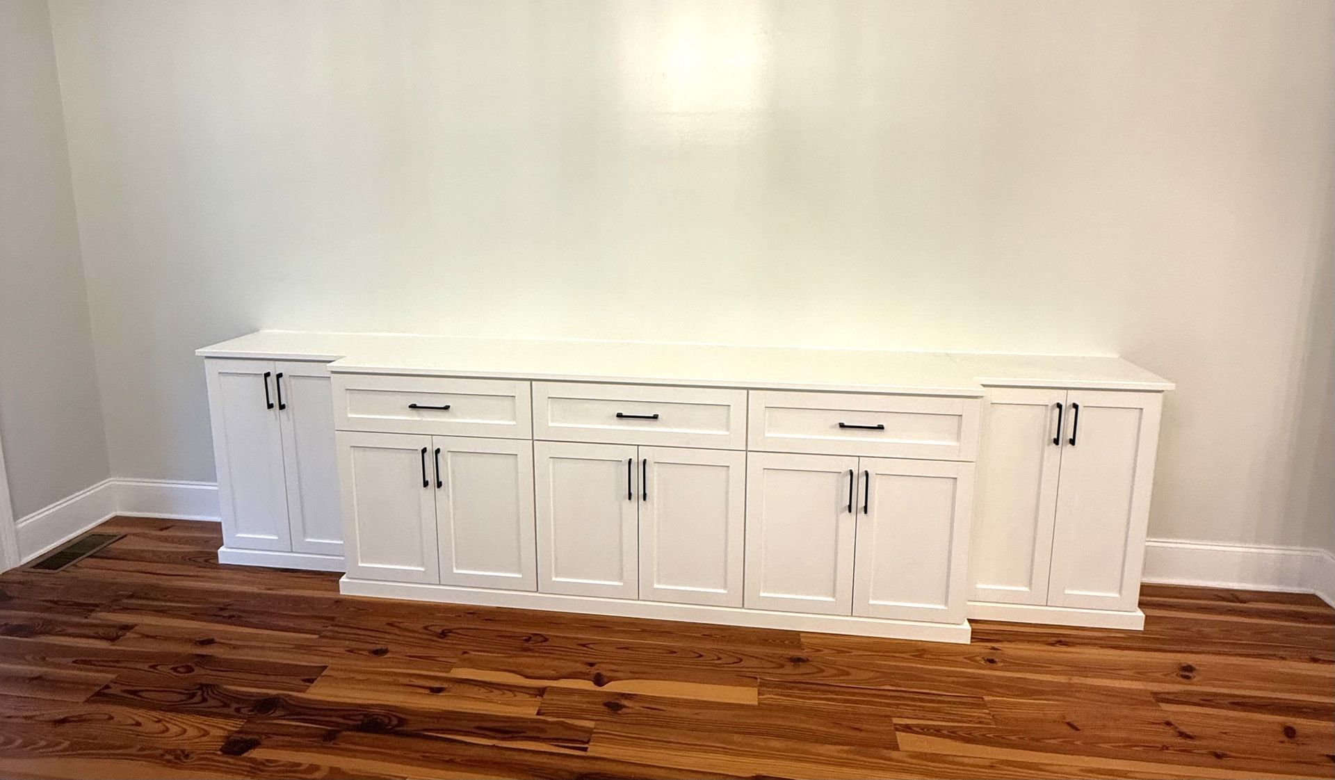 White cabinets with dark hardware against a white wall on a wood floor.