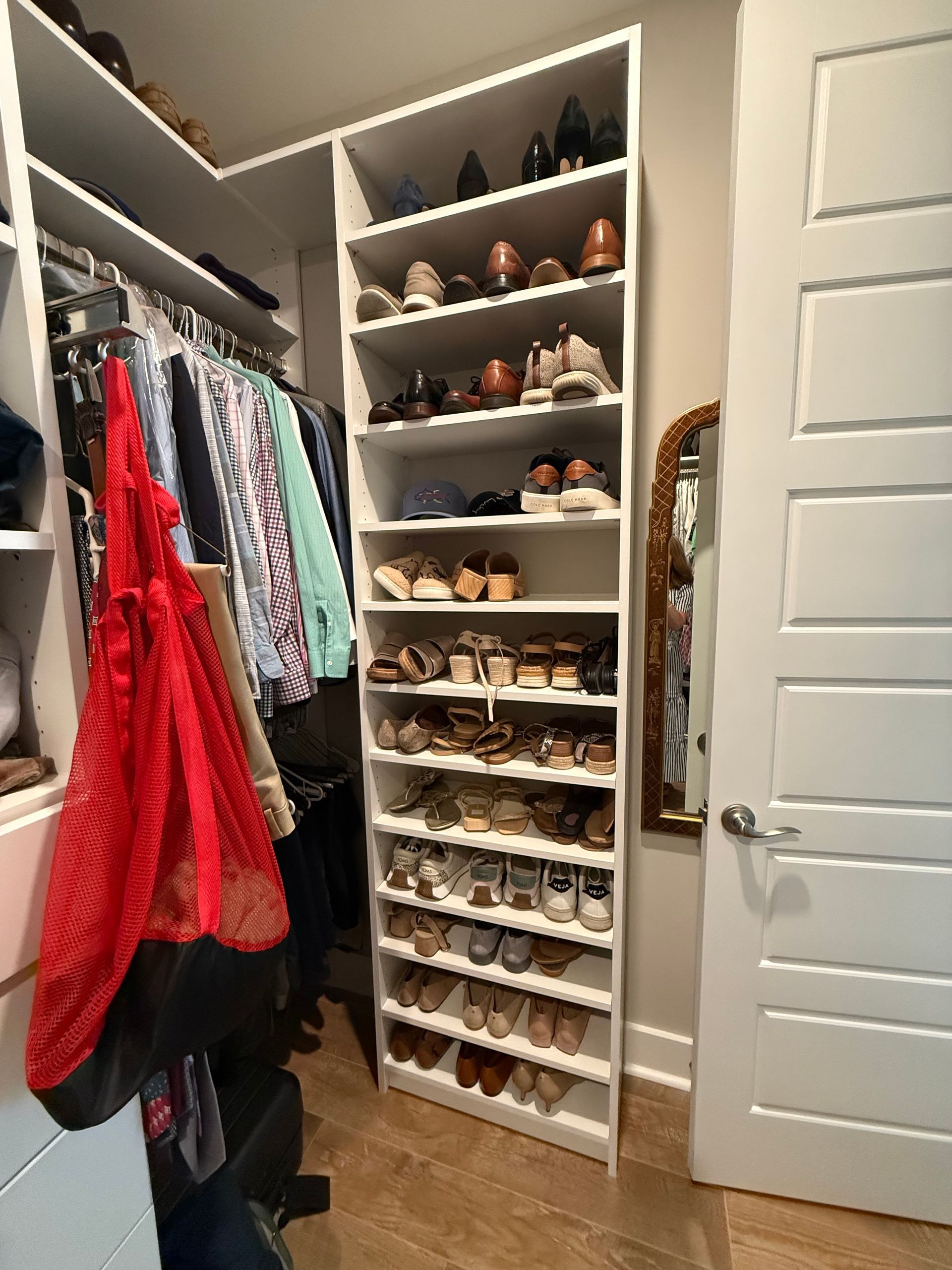 Closet with shoe shelves filled with footwear, adjacent to hanging clothes, near a door and mirror.