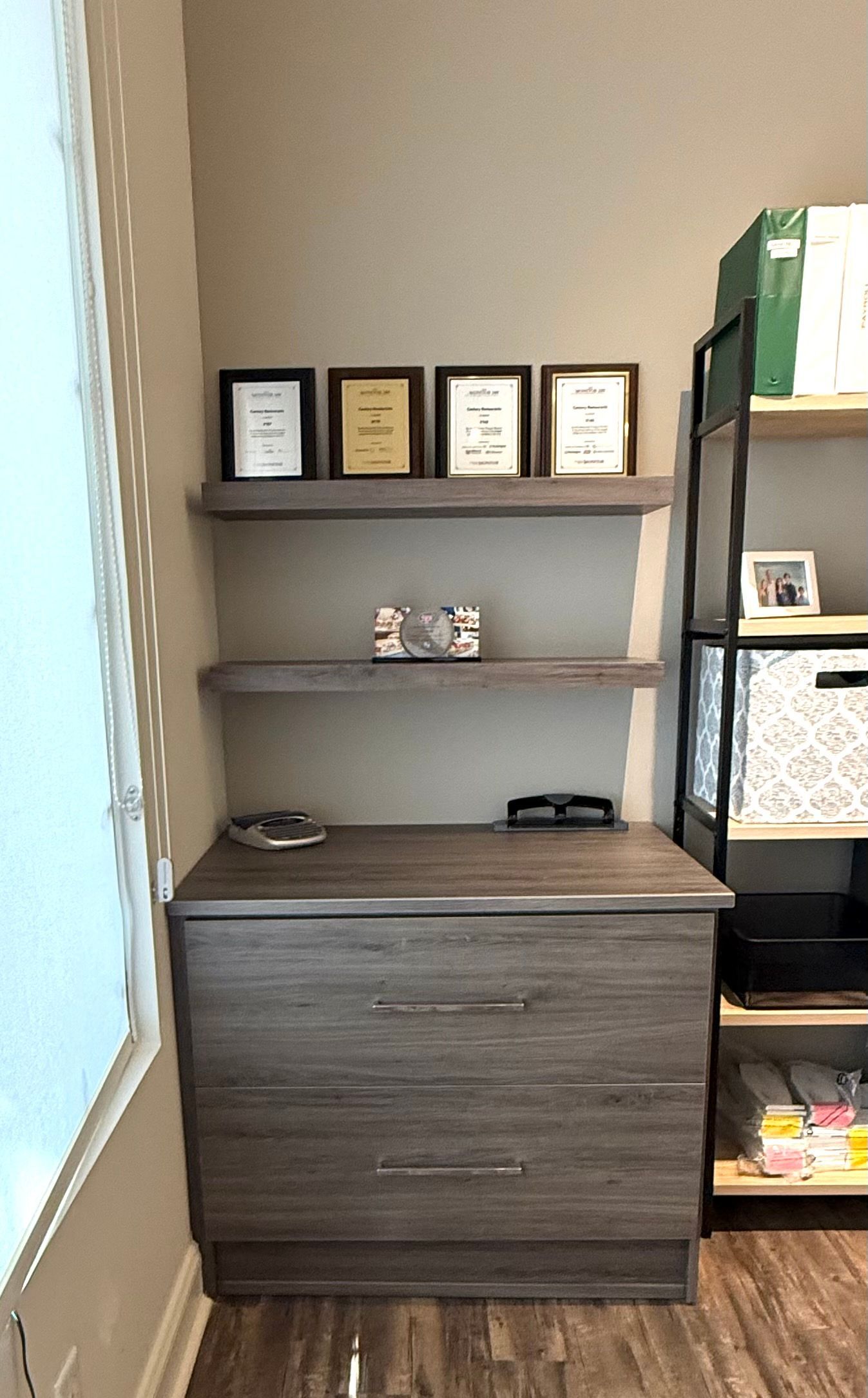 Wooden shelves with framed pictures and storage cabinet. A black metal shelf is to the right.