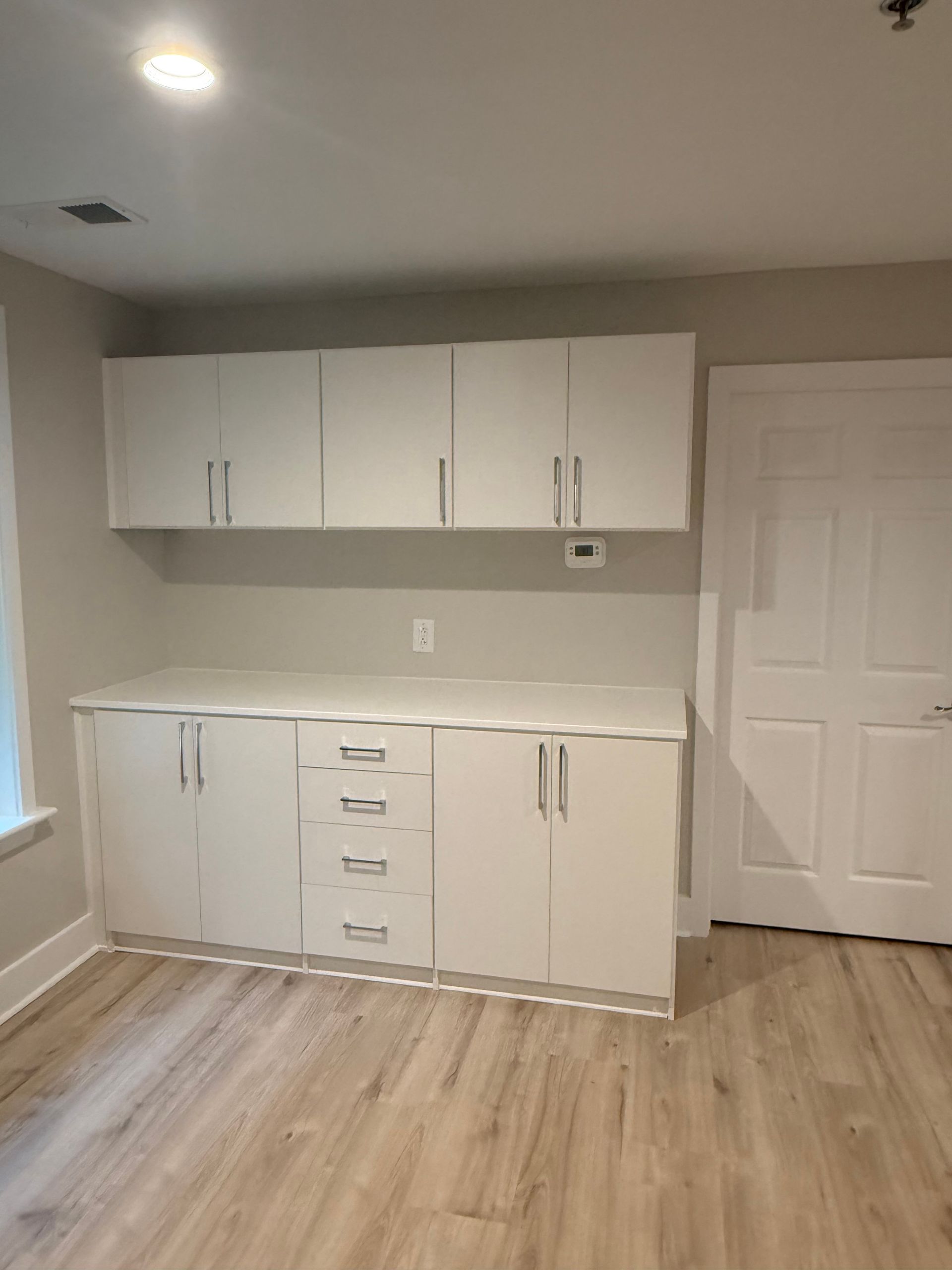 White cabinets with countertop, and door on wall of room with light flooring.