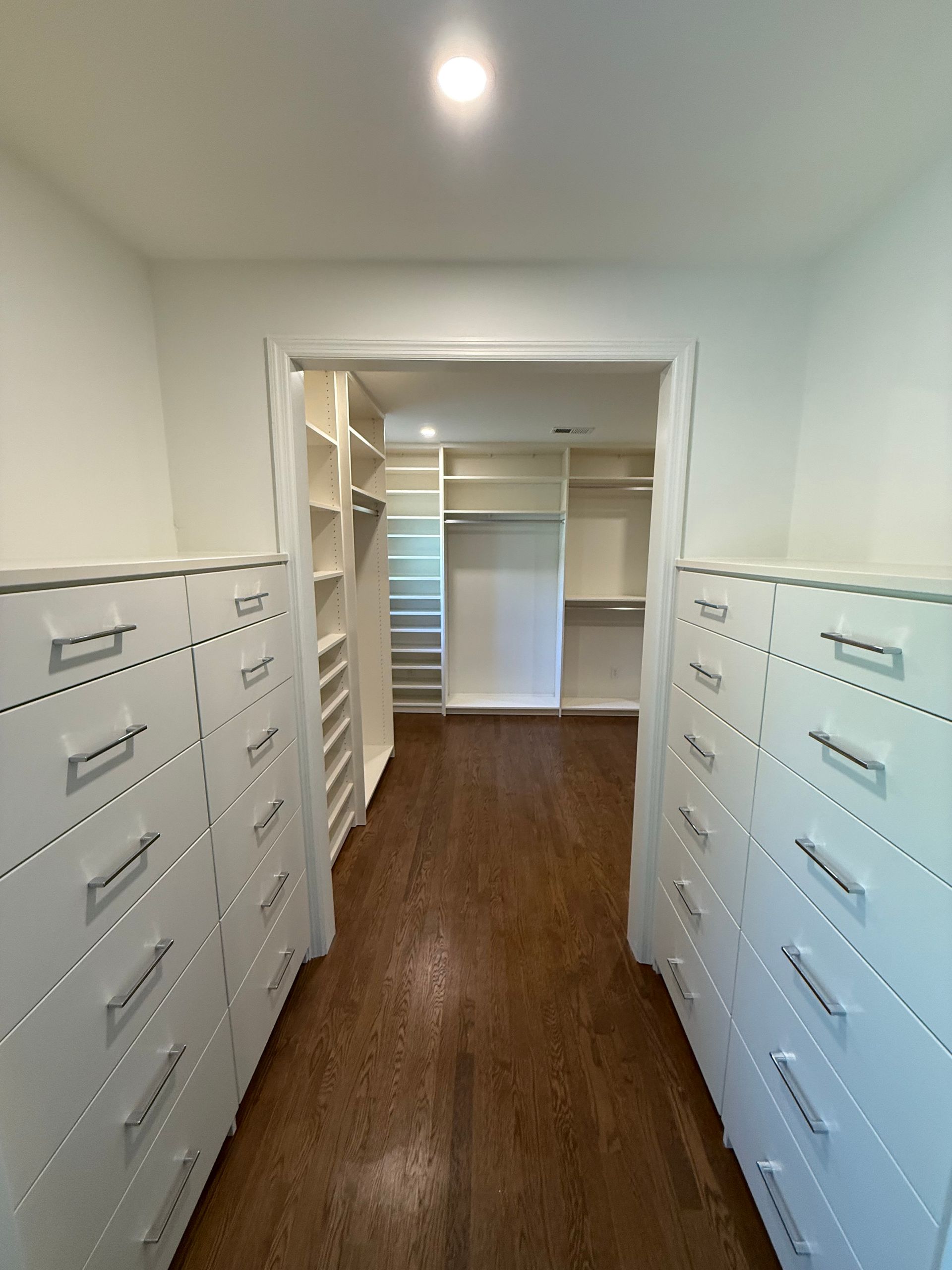 Walk-in closet with white drawers and shelves, dark wood floor. Light streams from the opening.