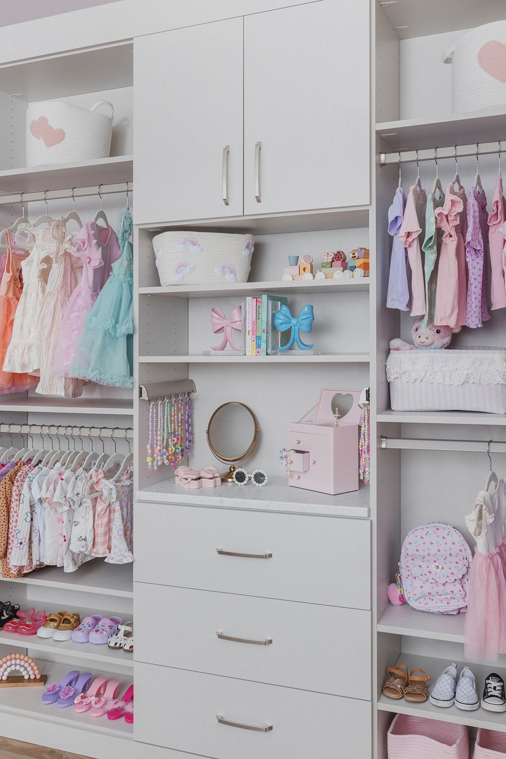 White bedroom closet with shelves and drawers, neatly organized with pastel clothes, shoes, toys, and accessories