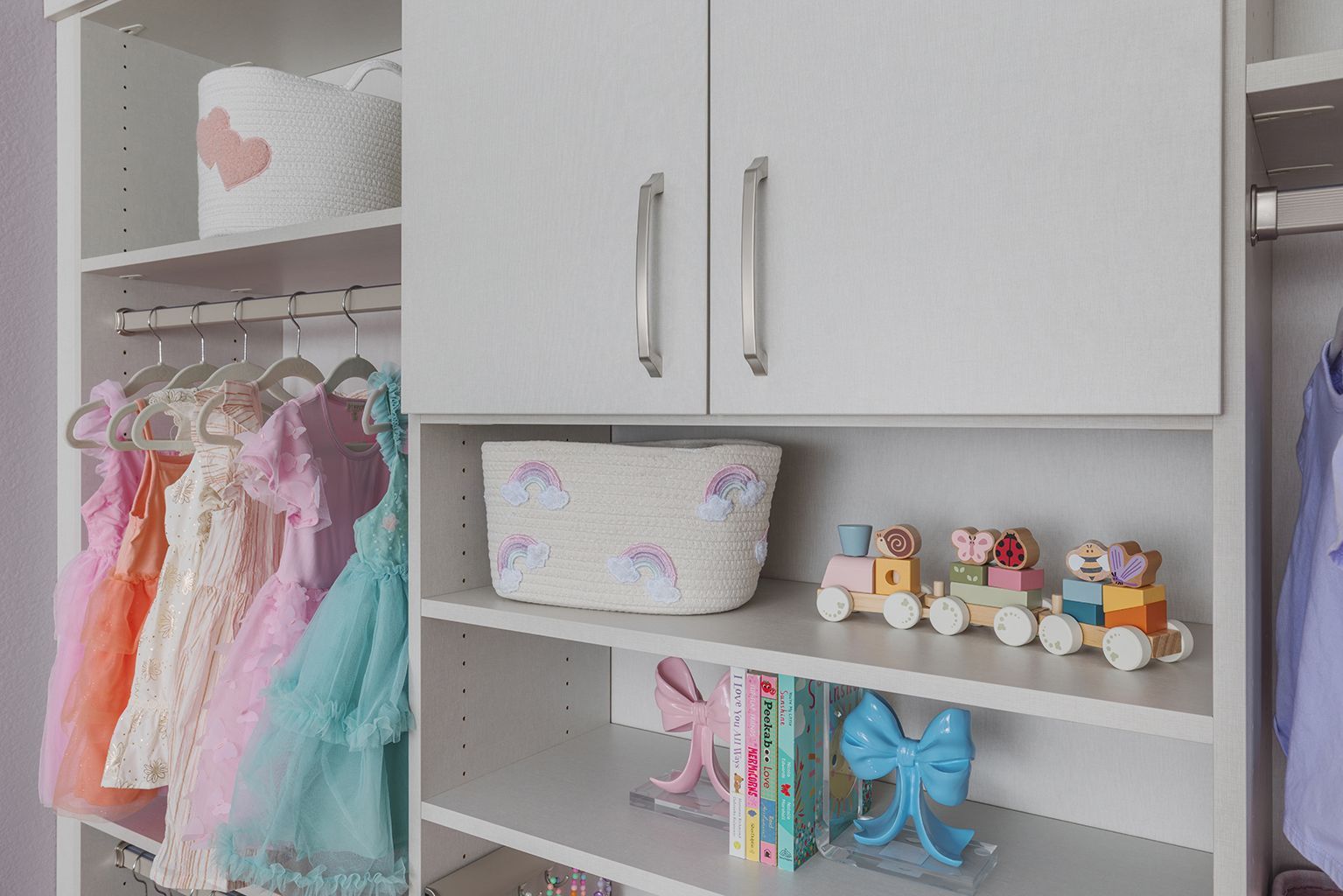 Children’s closet with hanging pastel dresses, shelves of toys, and white cabinets