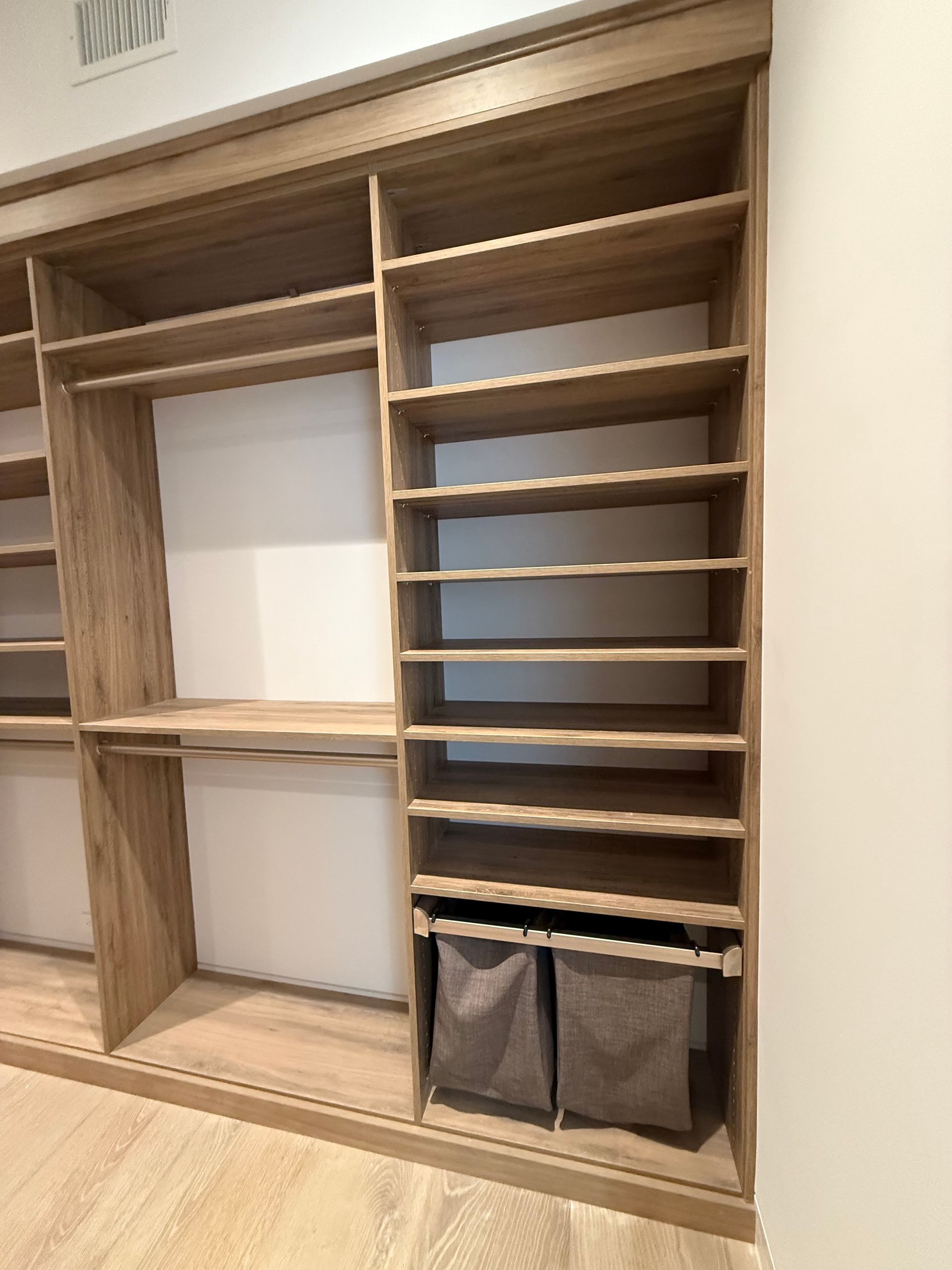 Wooden closet with shelves, hanging rods, and two fabric storage bins.