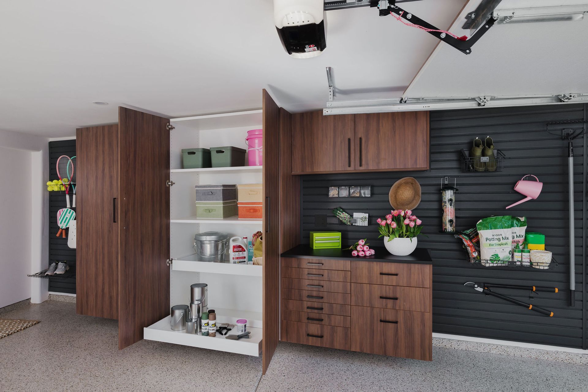 Garage storage area with wooden cabinets, open shelving, and assorted household items on a black wall.
