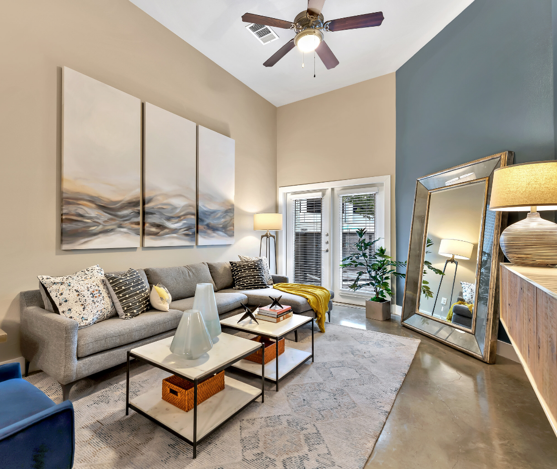 A living room with a couch , coffee table , mirror and ceiling fan.