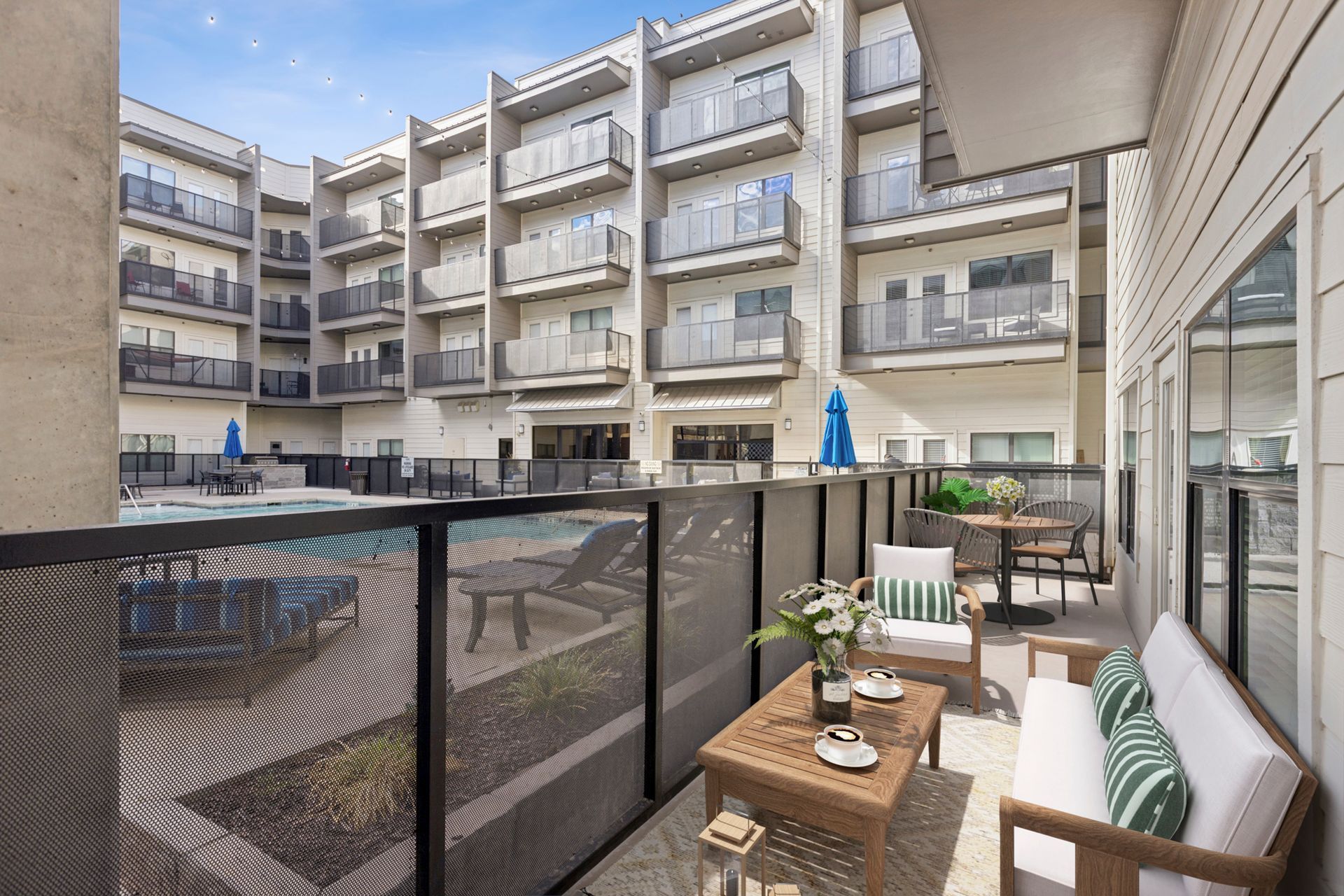 Balcony with patio furniture overlooking a pool and multi-story building.