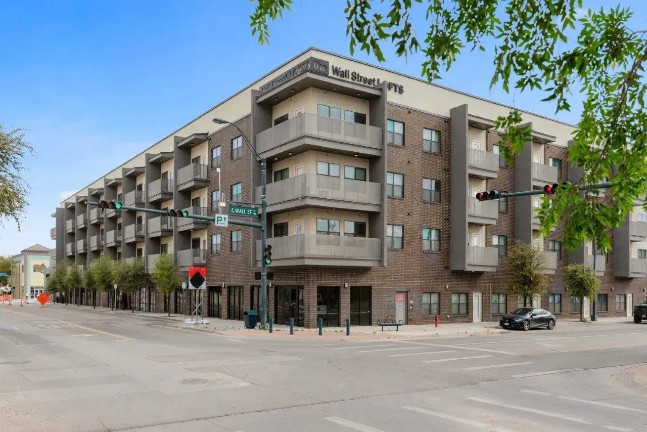 A large apartment building is sitting on the corner of a city street.