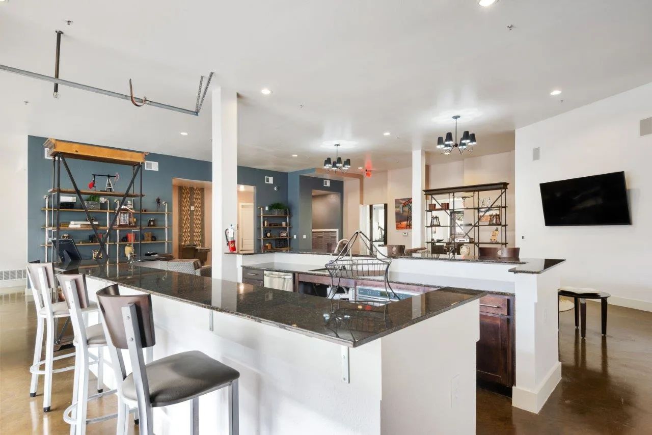 A kitchen with a large island and stools and a flat screen tv.