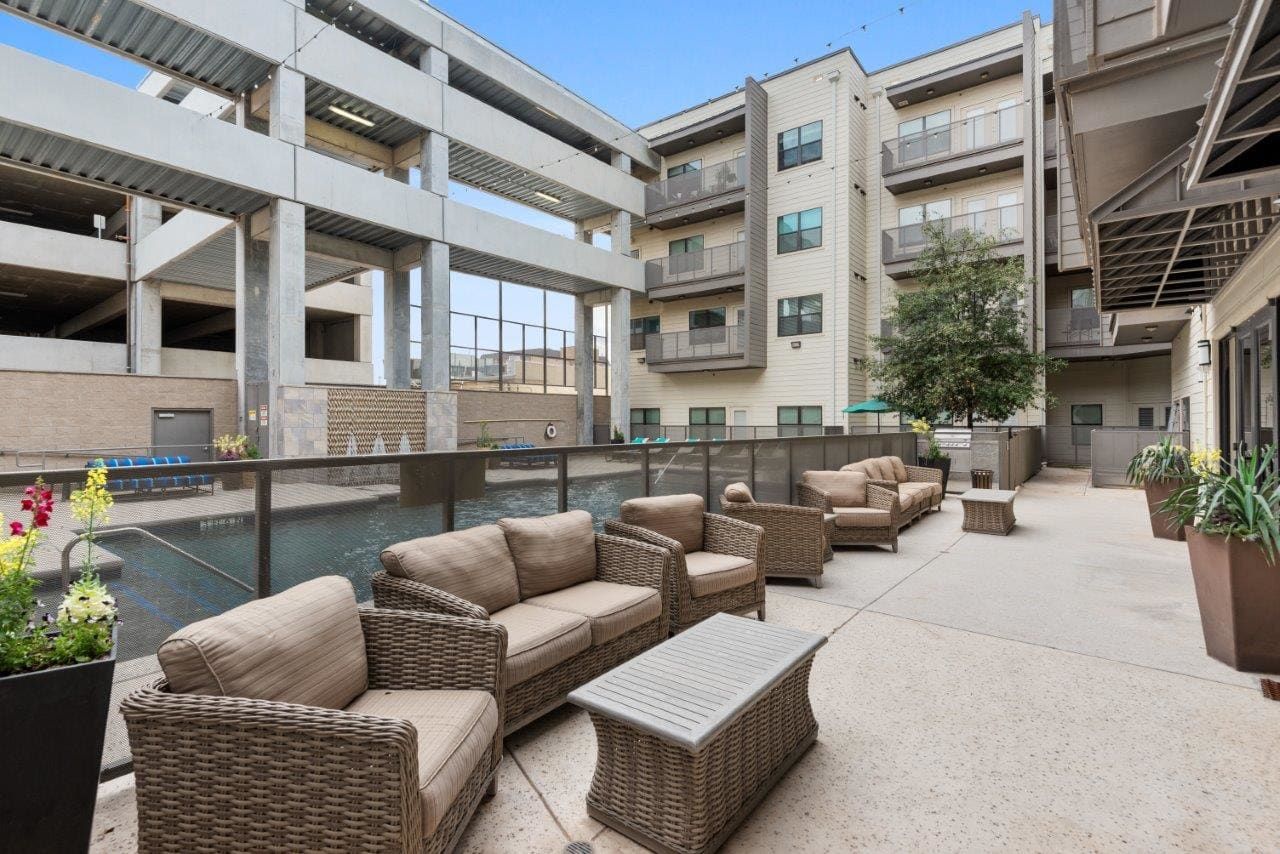 A patio with wicker furniture and a pool in front of a building.