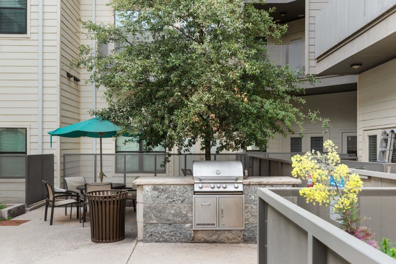 A patio with a grill and umbrellas in front of a building.