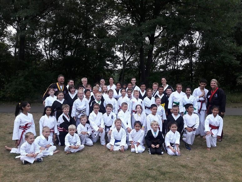A large group of children and adults wearing martial arts uniforms standing in a park for a group photo.