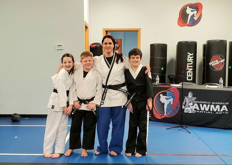 Four people in martial arts uniforms stand together smiling in a training studio with black practice bags in the background.