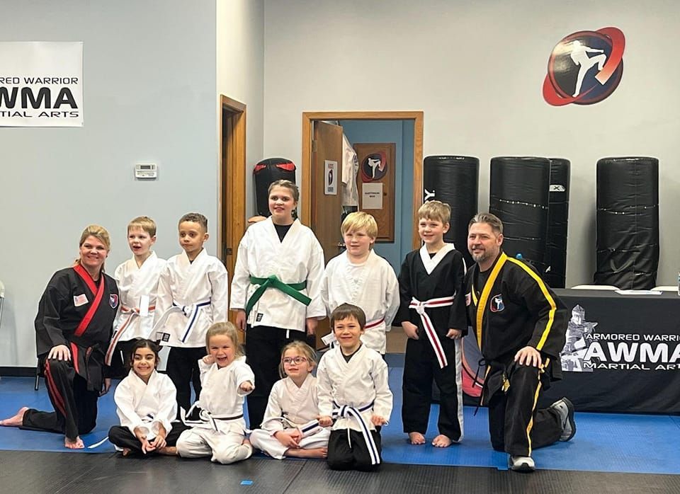 A group of martial arts students and two instructors in uniform pose for a photo in a training studio.