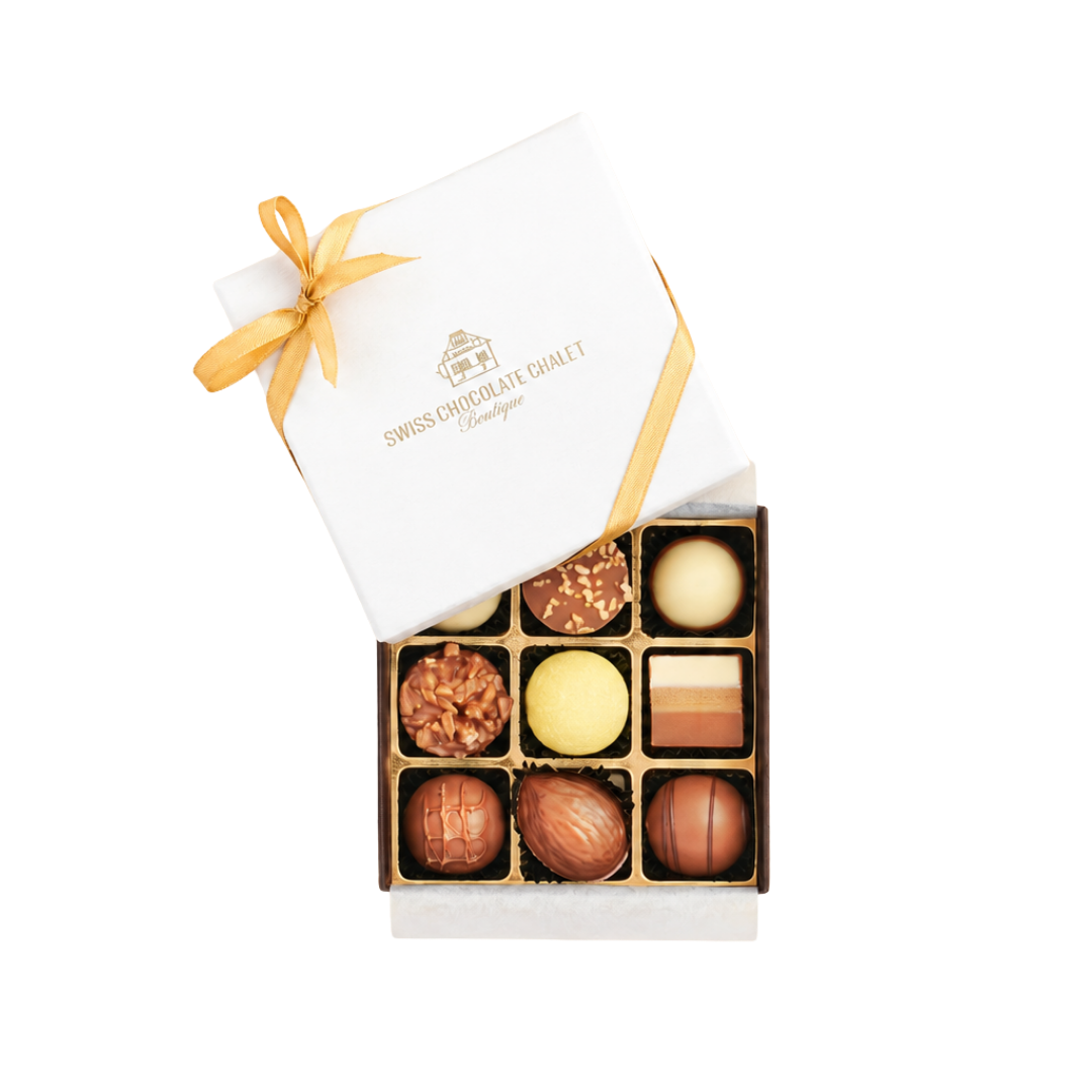 Weiße Geschenkbox mit goldenem Band, geöffnet, sodass darin verschiedene Pralinen in einer Schale zu sehen sind.