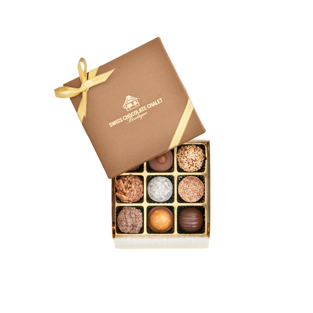 Braune Geschenkbox mit einer Auswahl an Pralinen und einer goldenen Schleife, der Deckel ist geöffnet und gibt den Blick auf die Pralinen im Inneren frei