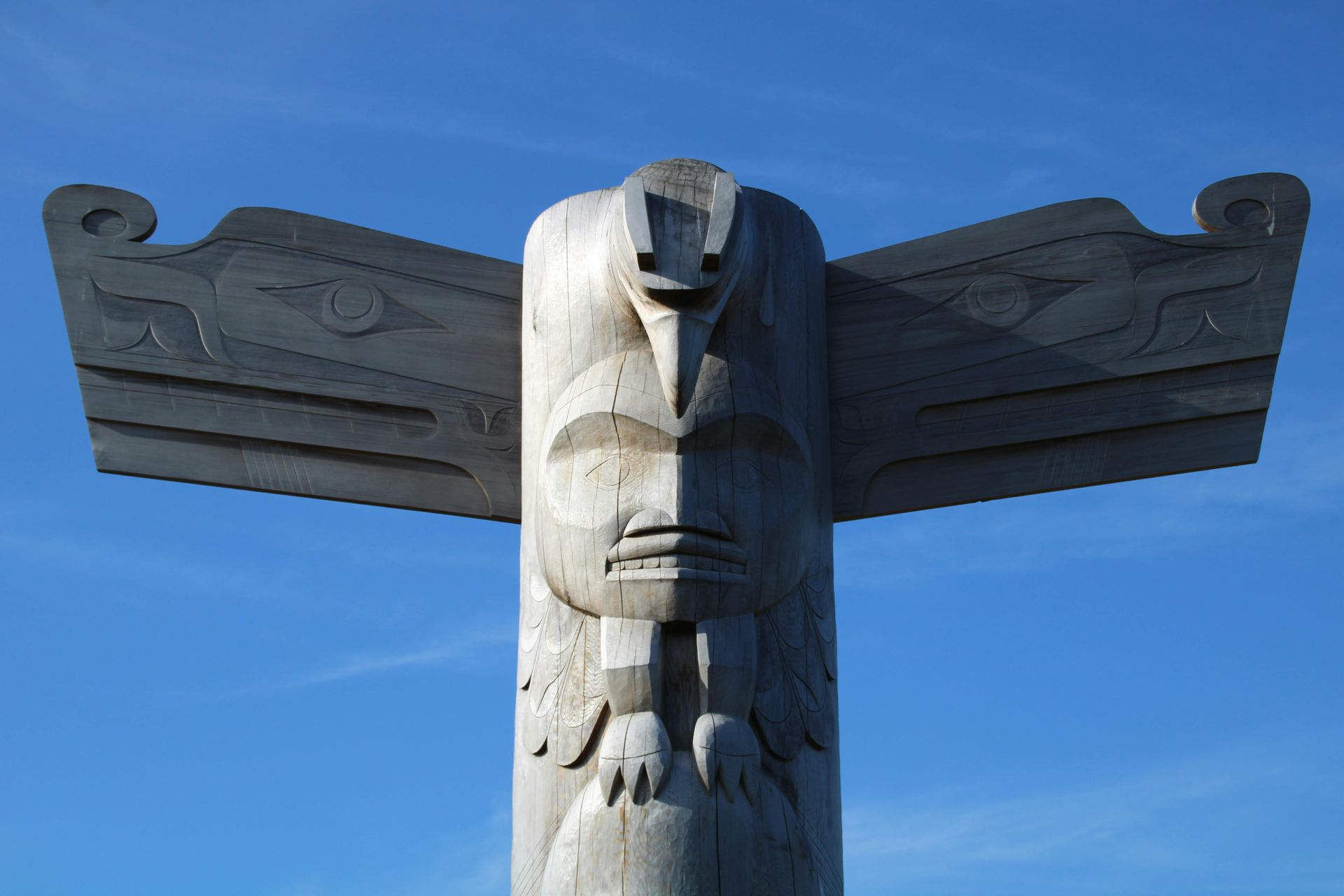 Totem pole with carved faces and spread wings, against a clear blue sky. Totem pole with carved faces and spread wings, against a clear blue sky.