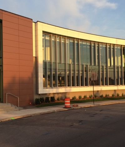 Modern building with curved glass windows, brown and white panels, and a red traffic cone in the foreground.