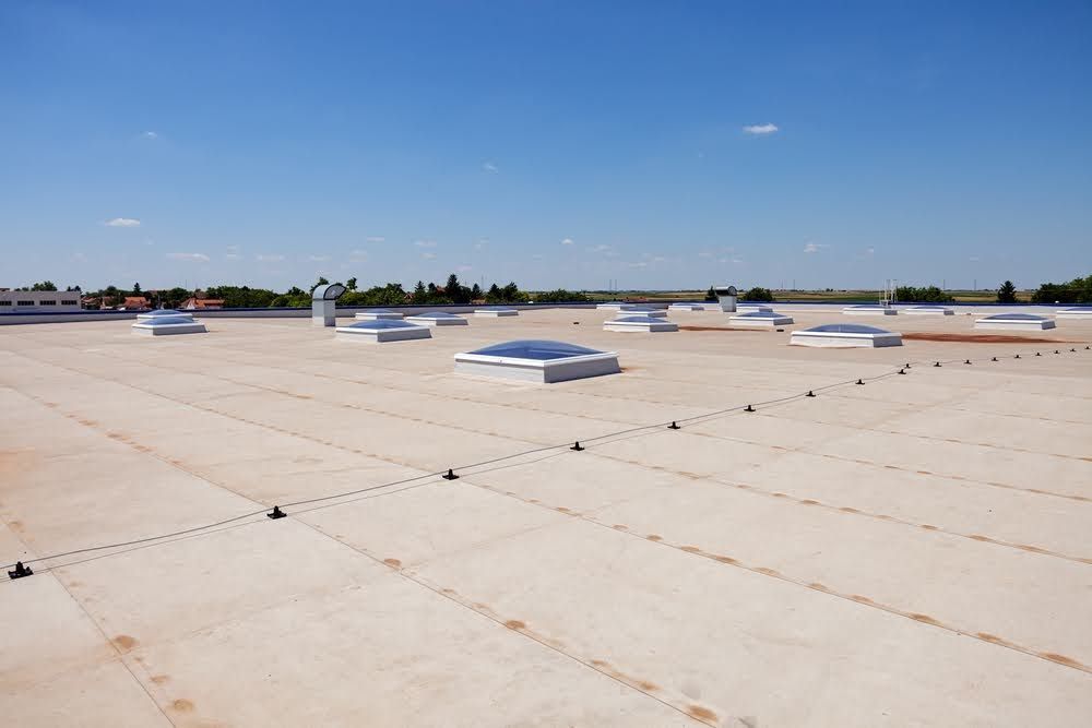 Flat commercial roof with skylights under a clear blue sky.
