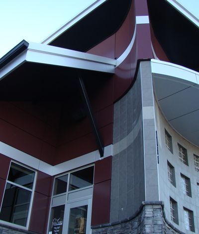 Exterior of a building with red and white accents, curved roof, glass windows, and stone base.