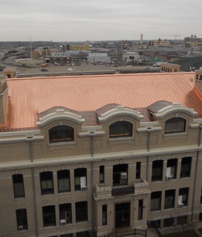 Building with copper roof and arched windows; city background.