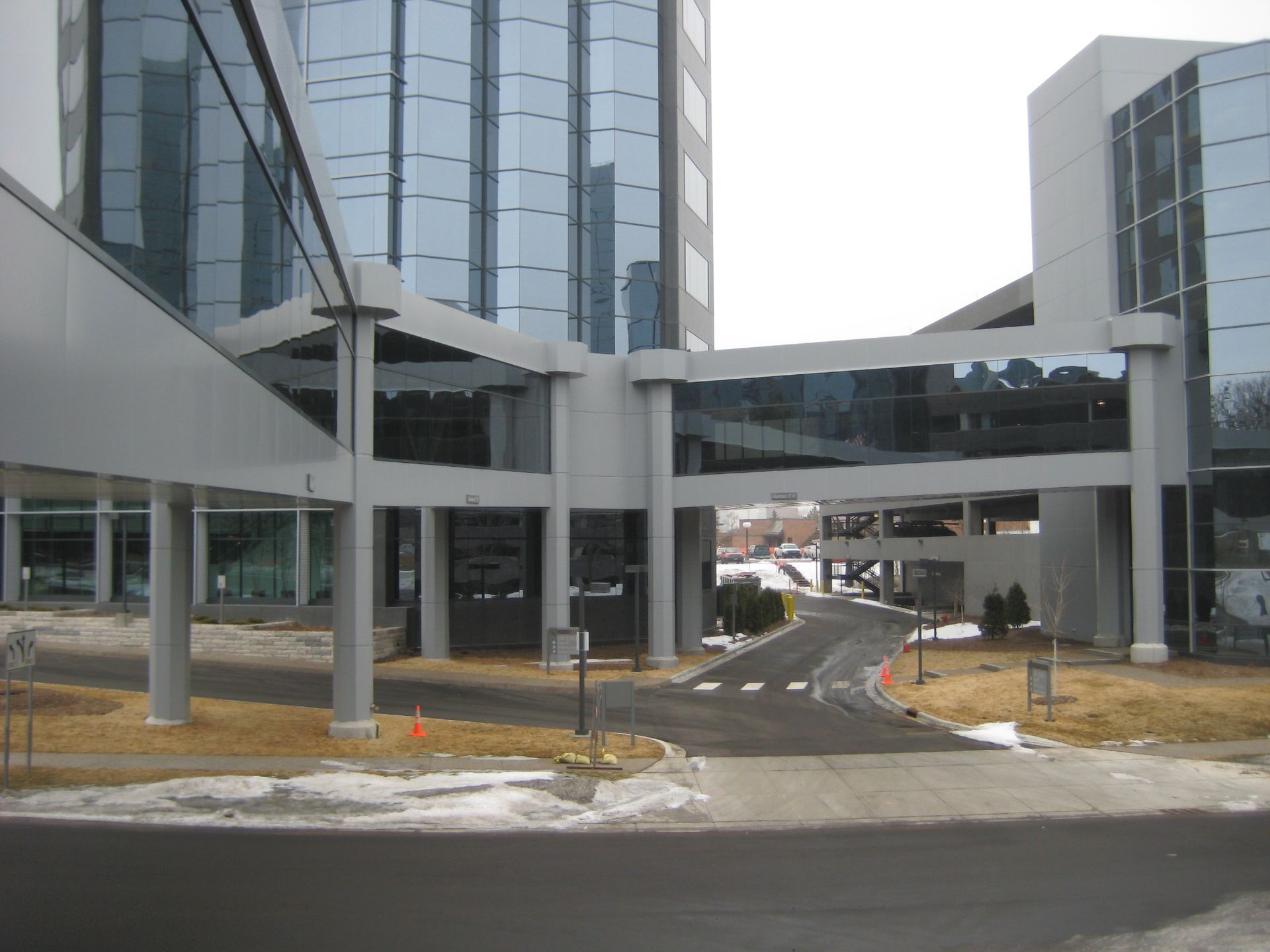 Sky bridges connect two modern buildings, over a roadway. Light gray and glass structures. Winter scene.