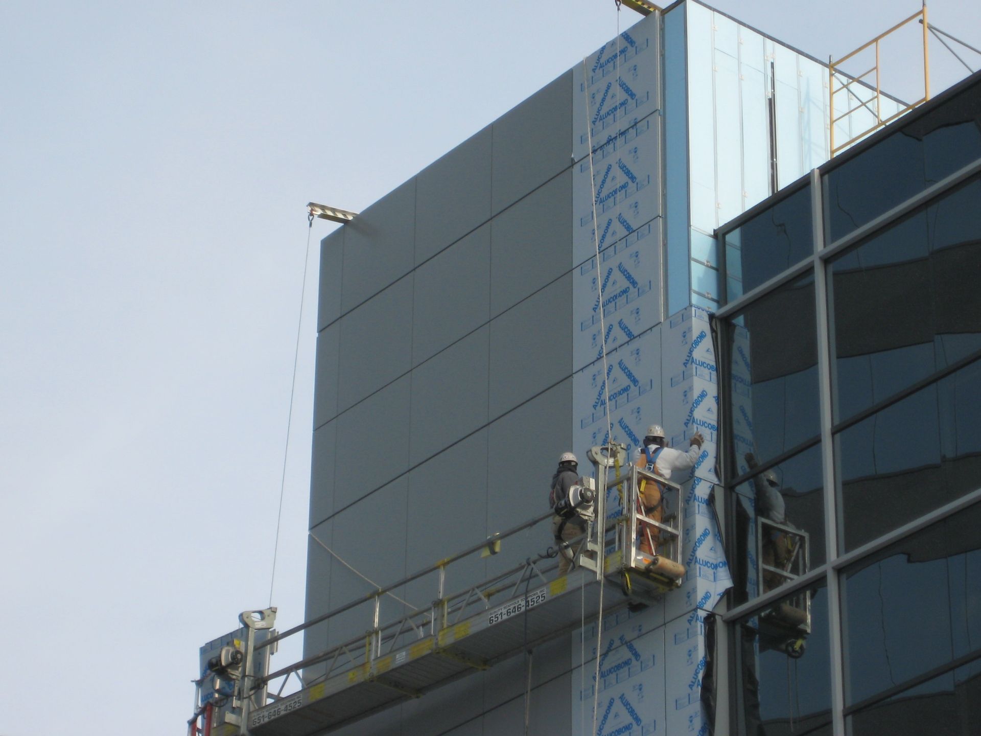 Construction workers in suspended platforms installing facade panels on a high-rise building.