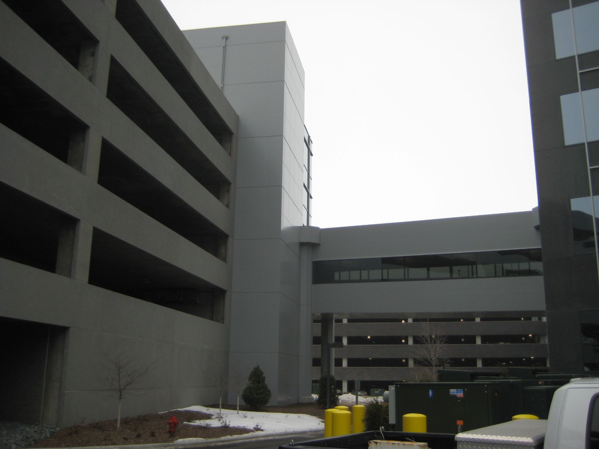 Grey parking garage connected to a building by a walkway; overcast sky.