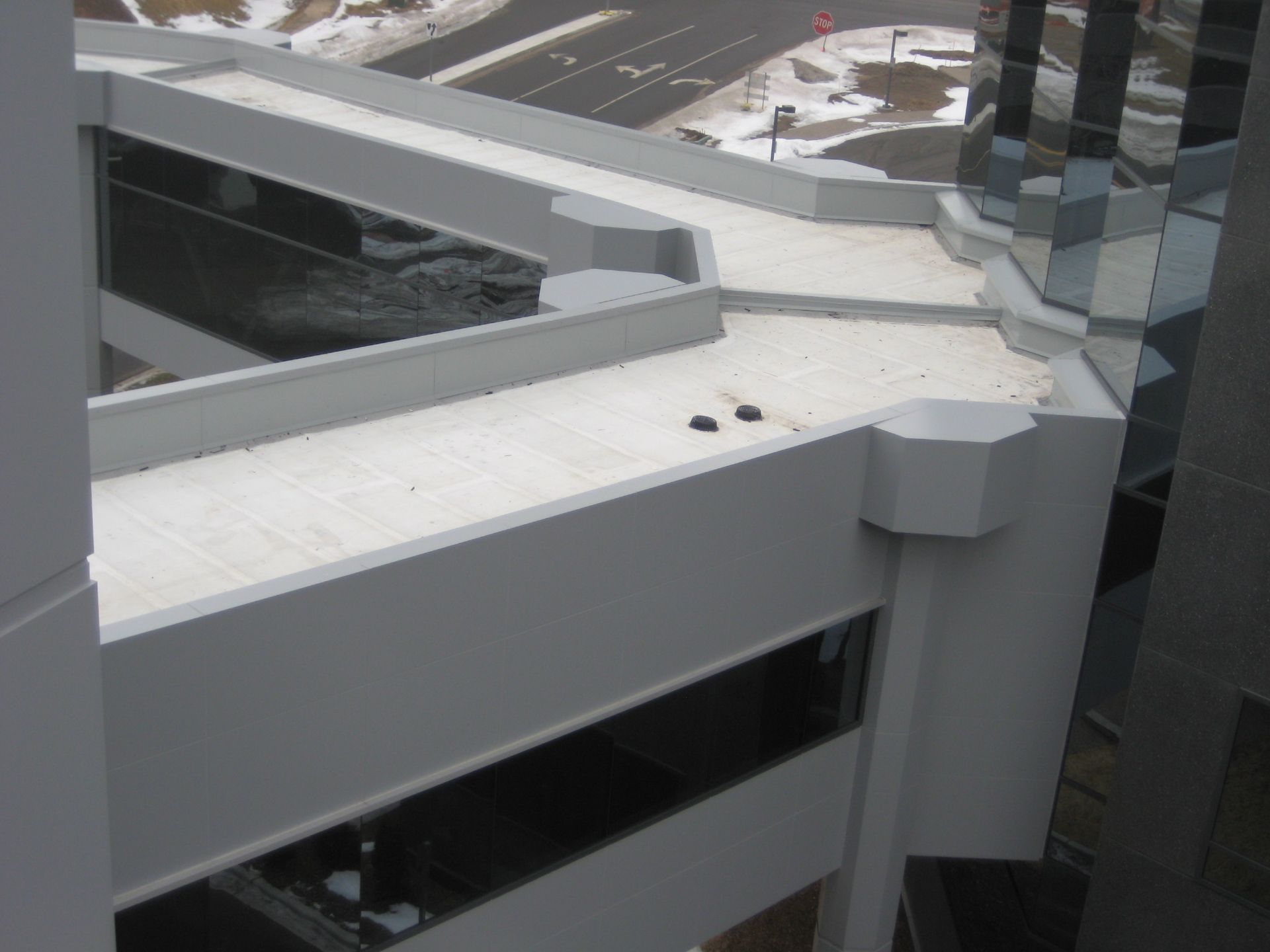 High-angle view of a white, multi-level building exterior with glass windows and a rooftop walkway.