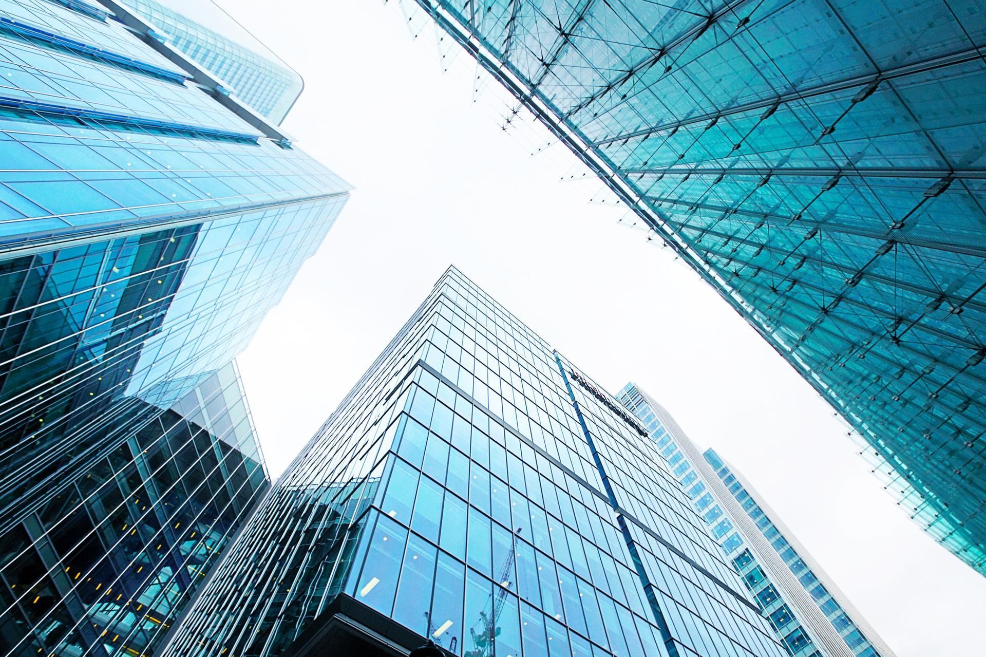 Glass skyscrapers reaching upwards, reflecting a blue sky.