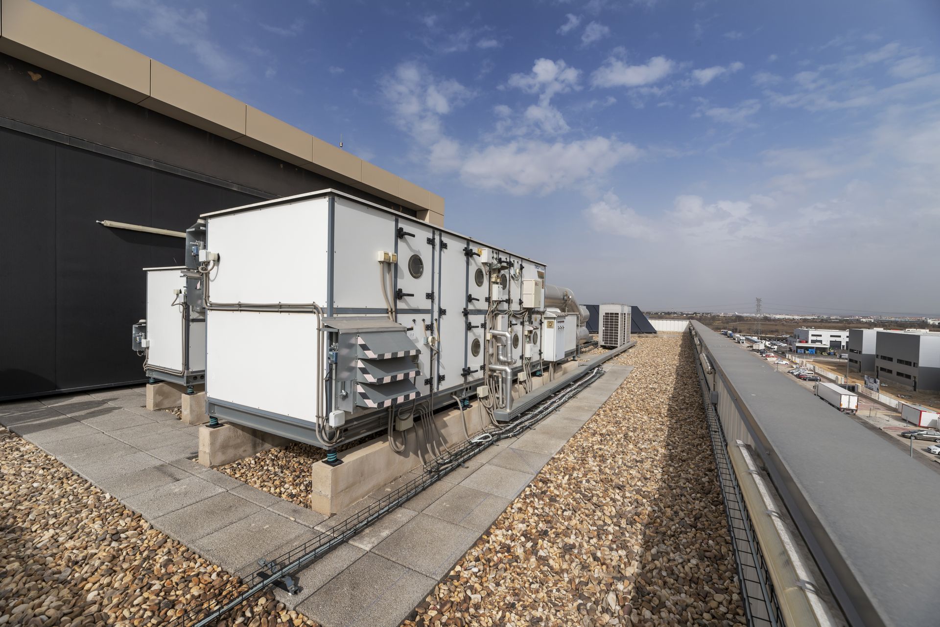 Rooftop HVAC units beside a building, with gravel and a distant city skyline under a blue sky.