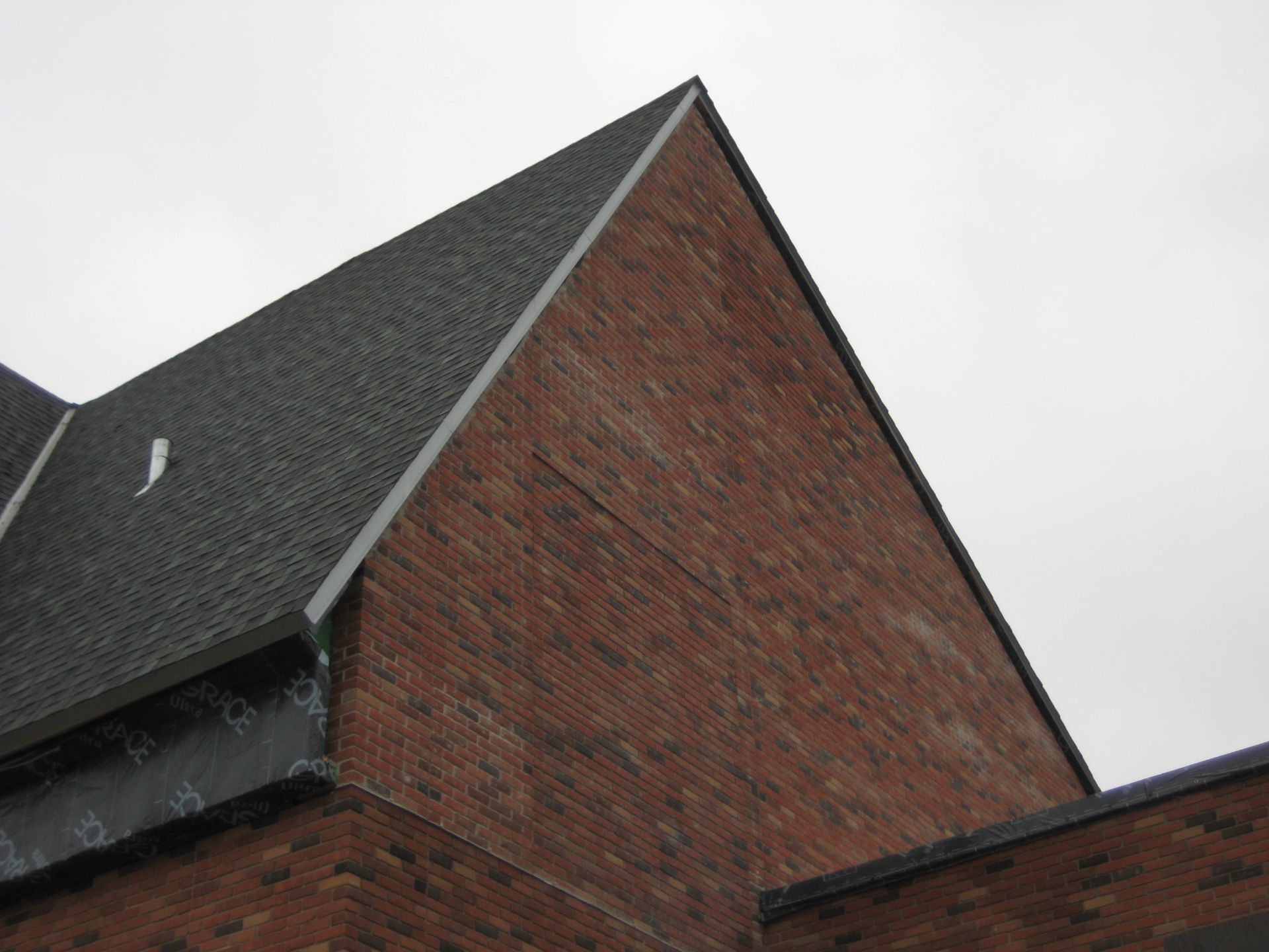 Brick building with dark shingled roof against a cloudy sky.