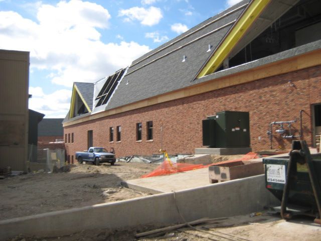 Construction site with a brick building and a sloped roof; a blue truck is parked nearby.