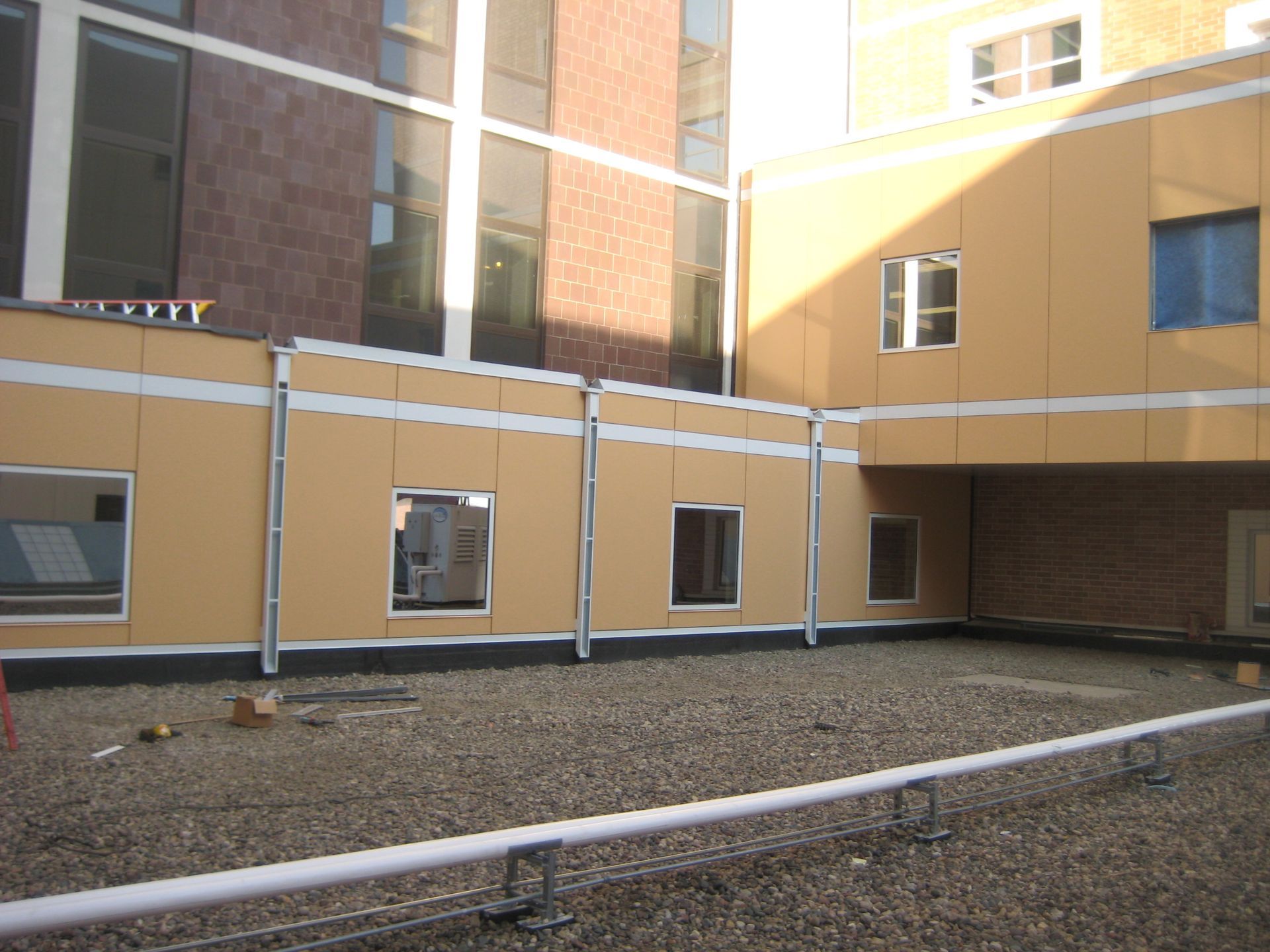 Exterior of a modern building with beige panels, windows, and gravel roofing, with metal handrail in foreground.