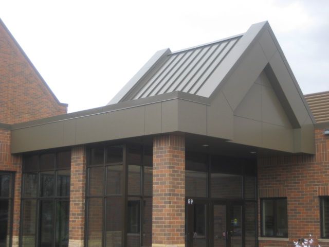 Brown building entrance with a gabled roof and metal siding. Brick facade and glass doors.