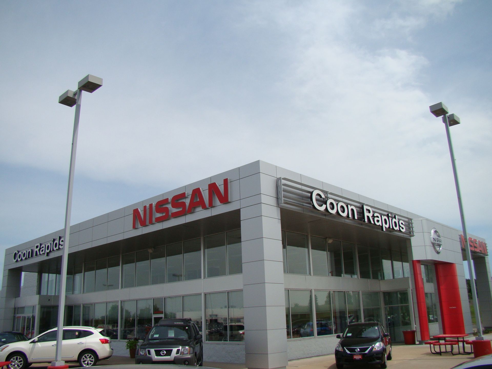 Nissan dealership in Coon Rapids, Minnesota, with building, cars, and cloudy sky.