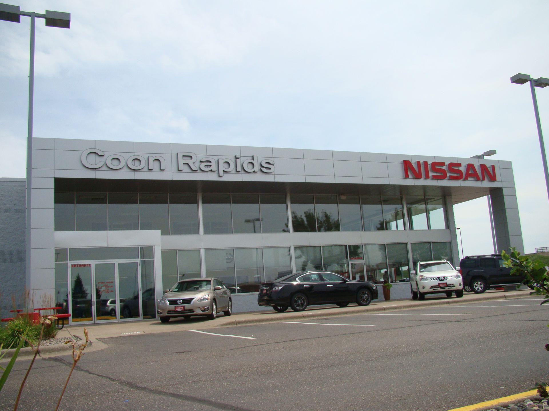 Coon Rapids Nissan dealership with glass facade, cars on display, and gray exterior.