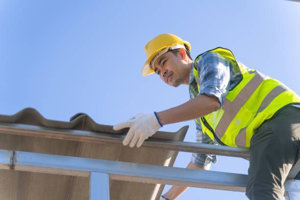 Roofer in yellow hard hat and vest inspecting a roof tile on a sunny day.