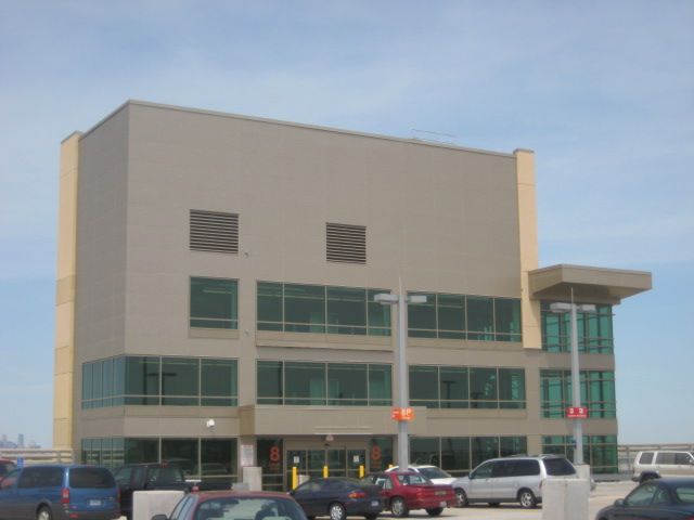 Beige rectangular building with glass windows, parked cars below, cloudy sky.
