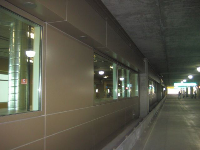 Long hallway with tan wall, windows, and bright lights, leading to a distant exit.